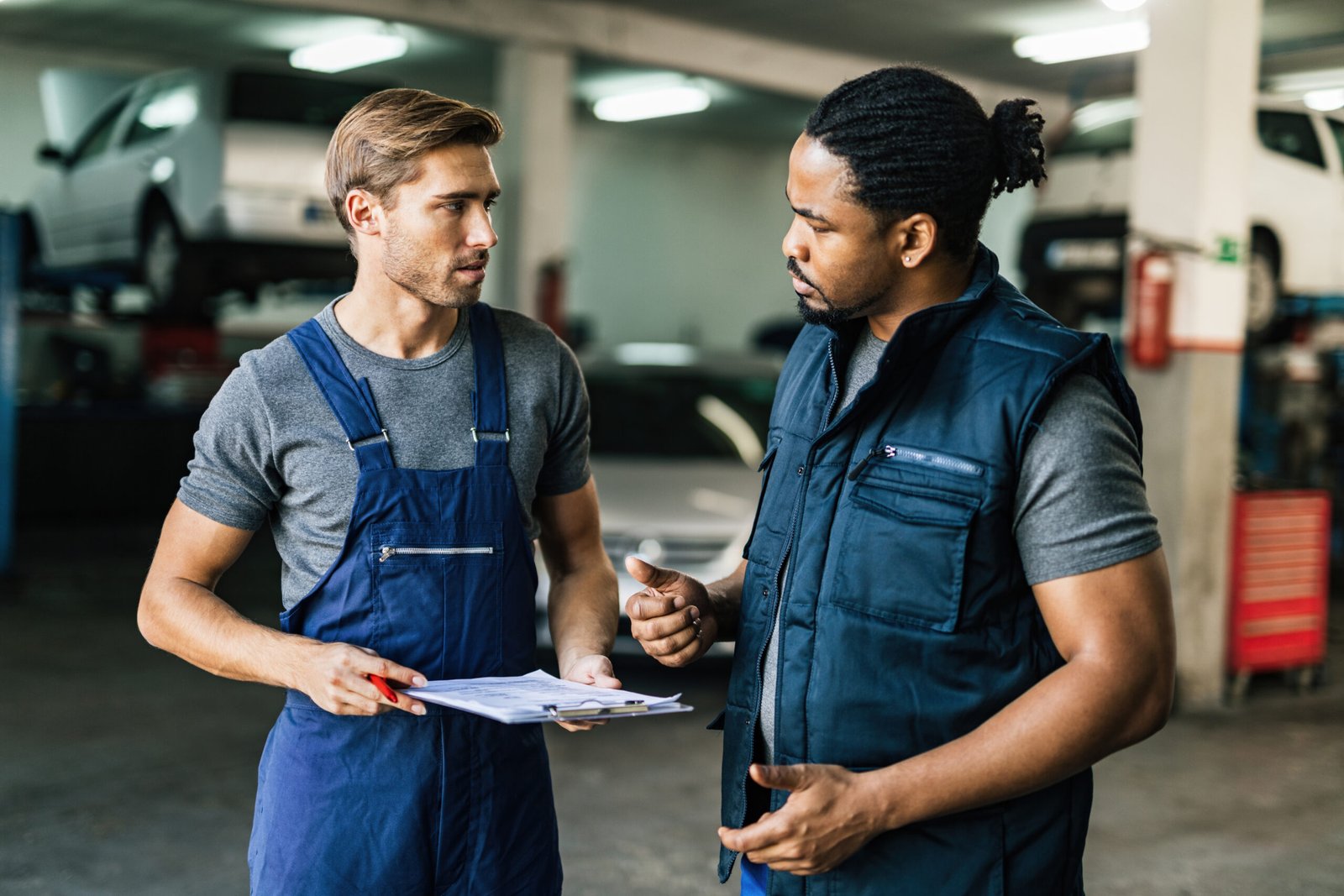 African American car mechanic and his coworker communicating in auto repair shop.